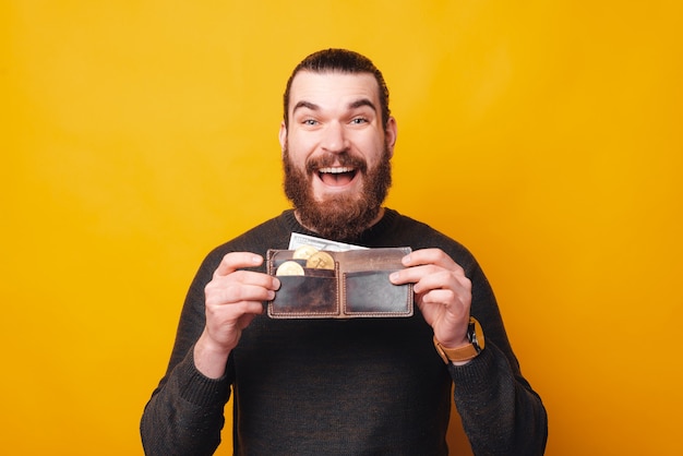 Un jeune homme heureux tient un portefeuille plein de bitcoins en souriant