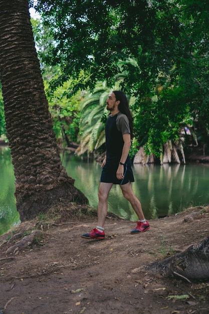 Jeune homme hippie latin marchant sur un sol nu dans une forêt avec lac Photo verticale