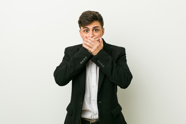 Jeune homme hispanique d'affaires choqué couvrant la bouche avec les mains.