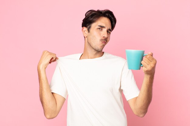 Jeune homme hispanique à l'air arrogant, réussi, positif et fier et tenant une tasse de café