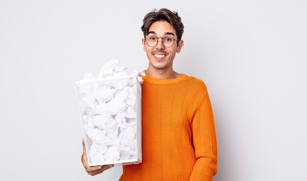 Jeune homme hispanique à l'air heureux et agréablement surpris. concept de poubelle de boules de papier