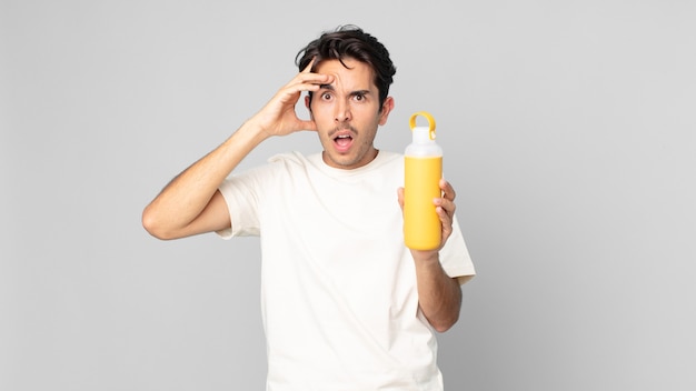 Jeune homme hispanique à l'air heureux, étonné et surpris avec un thermos de café