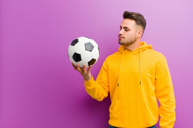 Jeune homme hispanique avec un ballon de football contre le mur violet