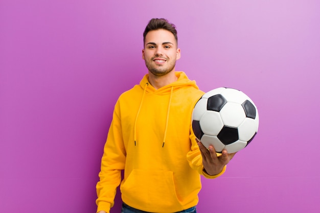 Jeune homme hispanique avec un ballon de football contre violet