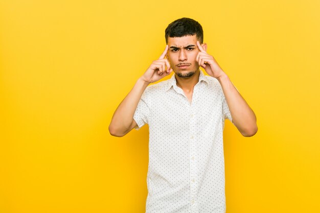 Jeune homme hispanique concentré sur une tâche, gardant les index pointant la tête.