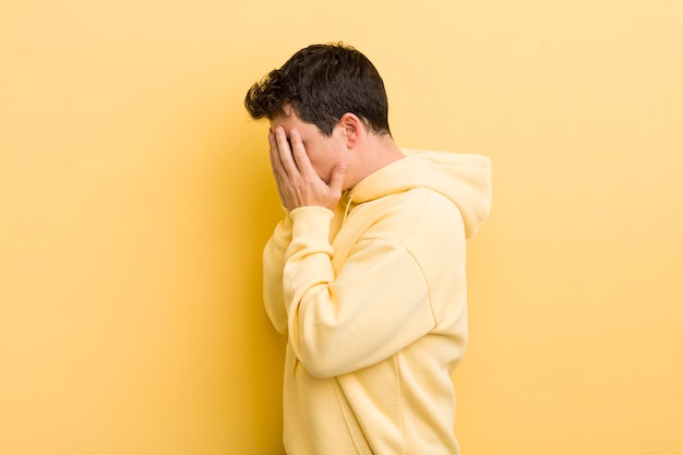 Jeune homme hispanique couvrant les yeux avec les mains avec un regard triste et frustré de désespoir pleurant vue latérale