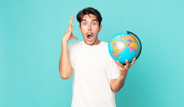 Jeune homme hispanique criant avec les mains en l'air et tenant une carte du globe terrestre