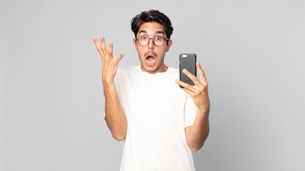 Jeune homme hispanique criant avec les mains en l'air et tenant un smartphone