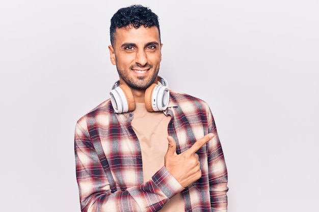 Jeune homme hispanique écoutant de la musique à l'aide d'un casque souriant joyeux pointant avec la main et le doigt sur le côté