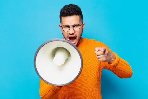 Jeune homme hispanique expression en colère et tenant un mégaphone