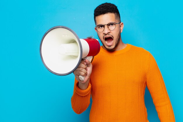 Jeune homme hispanique expression en colère et tenant un mégaphone