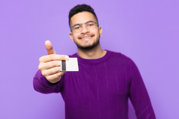 Jeune homme hispanique expression heureuse et tenant une carte de crédit