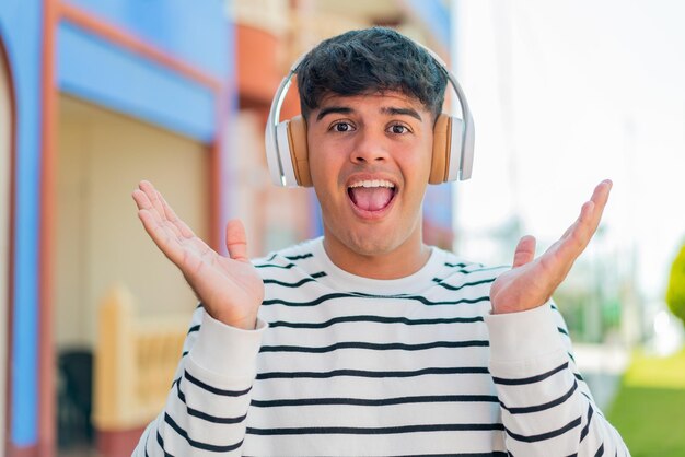 Photo jeune homme hispanique à l'extérieur surpris et écoutant de la musique