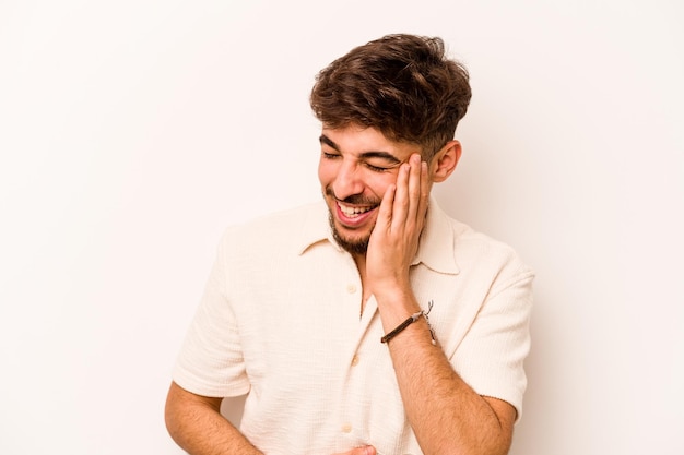 Jeune homme hispanique isolé sur fond blanc rit joyeusement et s'amuse à garder les mains sur le ventre