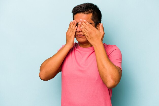 Jeune homme hispanique isolé sur fond bleu peur couvrant les yeux avec les mains