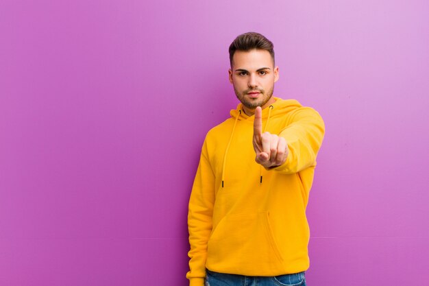 Jeune homme hispanique avec un look décontracté contre le mur violet