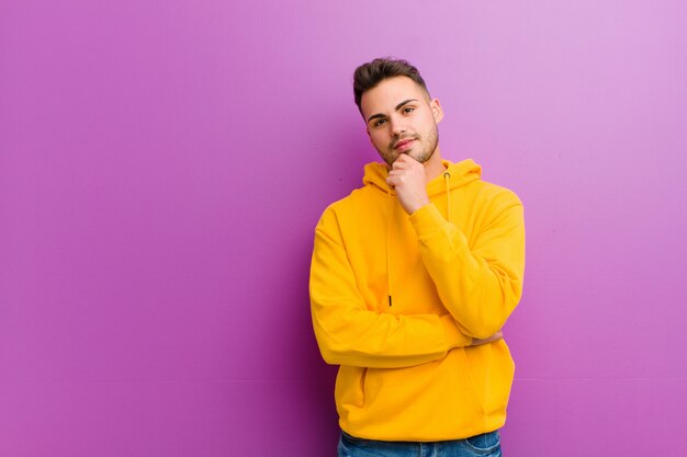 Jeune homme hispanique avec un look décontracté contre le mur violet