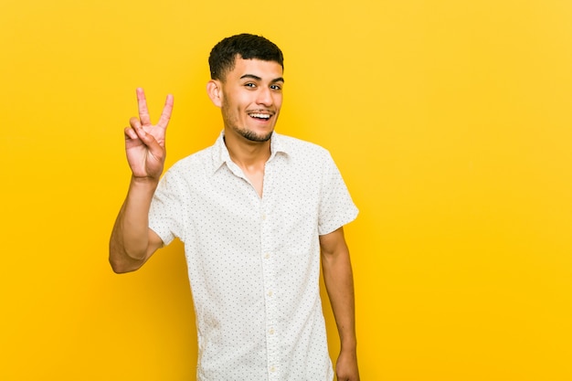 Jeune homme hispanique montrant le signe de la victoire et souriant largement.