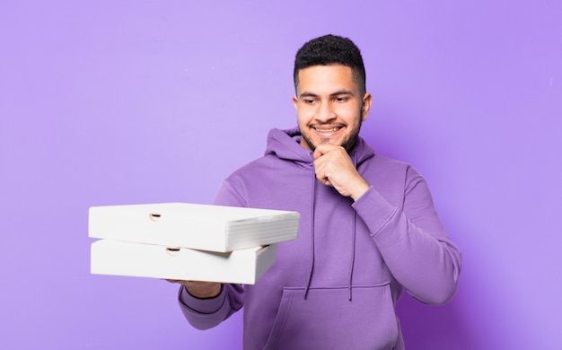 Jeune homme hispanique pensant à l'expression et tenant des pizzas à emporter