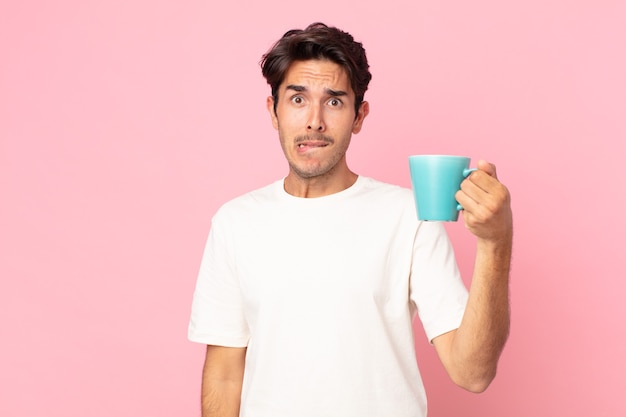 Jeune homme hispanique à la perplexité et confus et tenant une tasse de café