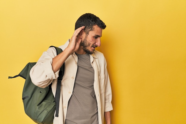 Jeune homme hispanique avec un sac à dos essayant d'écouter un commérage