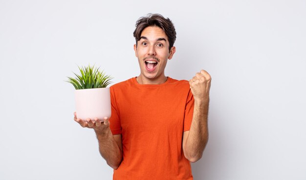 Jeune homme hispanique se sentant choqué, riant et célébrant le succès. concept de plante décorative