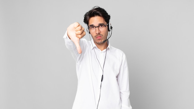 Jeune homme hispanique se sentant croisé, montrant les pouces vers le bas. concept de télévendeur