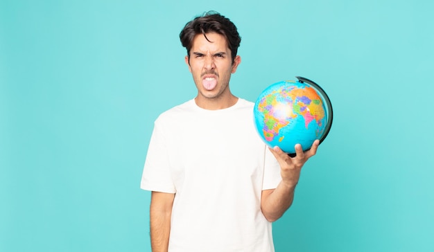 Jeune homme hispanique se sentant dégoûté et irrité et la langue et tenant une carte du globe terrestre