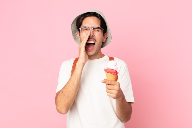 Jeune homme hispanique se sentant heureux, donnant un grand cri avec les mains à côté de la bouche et tenant une glace