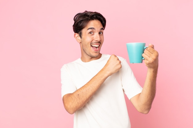 Jeune homme hispanique se sentant heureux et faisant face à un défi ou célébrant et tenant une tasse de café