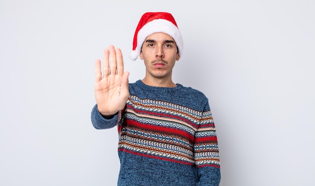 Jeune homme hispanique à la sérieuse montrant la paume ouverte faisant un geste d'arrêt. concept de nouvel an et noël