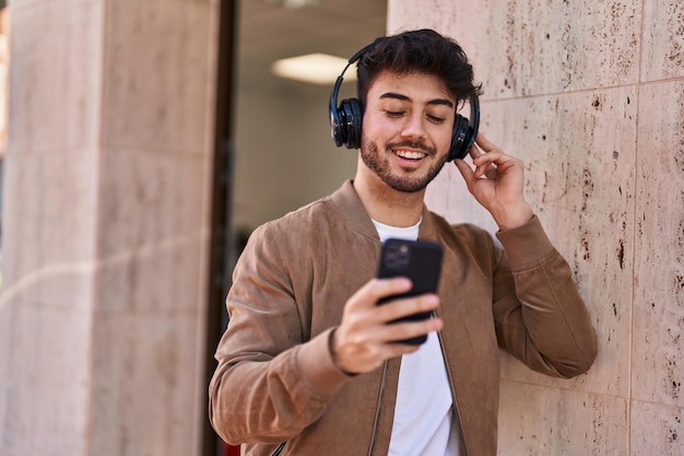 Jeune homme hispanique souriant confiant écoutant de la musique dans la rue