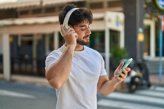 Jeune homme hispanique souriant confiant écoutant de la musique dans la rue