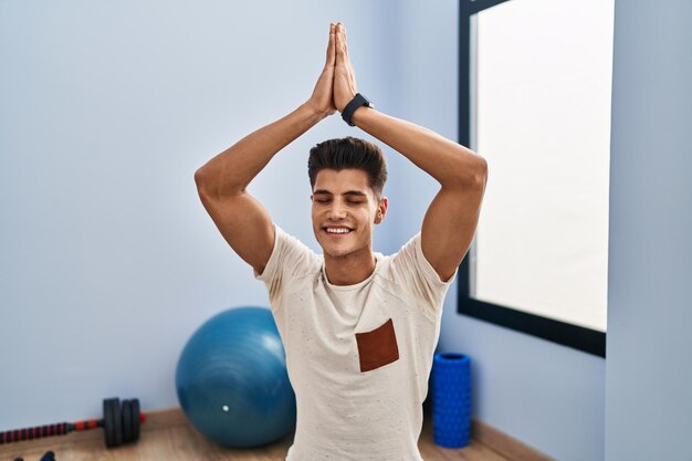 Jeune homme hispanique souriant formation yoga confiant au centre sportif