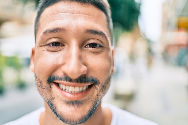 Jeune homme hispanique souriant heureux marchant dans la rue de la ville.