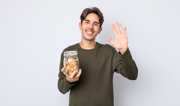 Jeune homme hispanique souriant joyeusement, agitant la main, vous accueillant et vous saluant. notion de biscuits