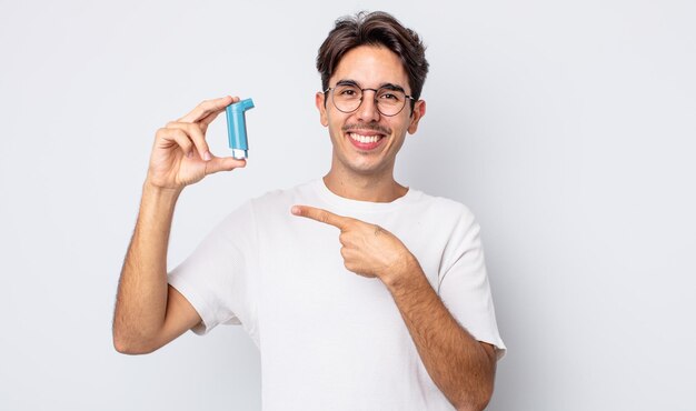 Jeune homme hispanique souriant joyeusement, se sentant heureux et pointant sur le côté. concept d'asthme