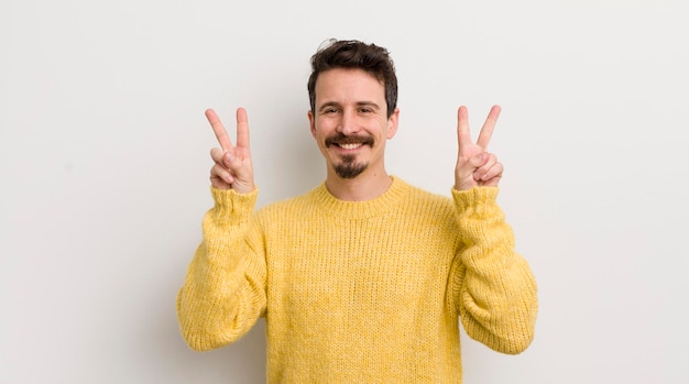 Jeune homme hispanique souriant et regardant heureux amical et satisfait gestant la victoire ou la paix avec les deux mains