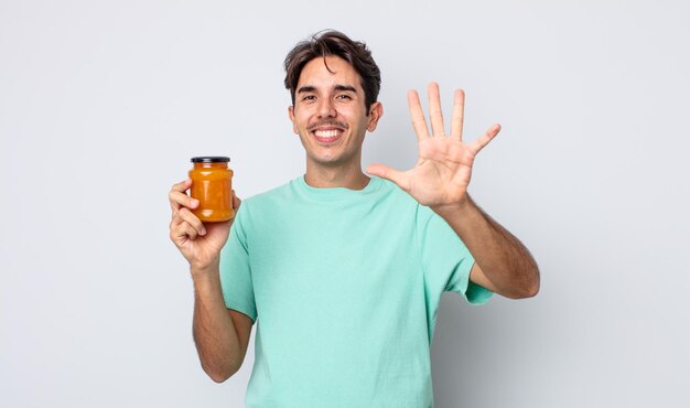 Jeune homme hispanique souriant et semblant amical, montrant le numéro cinq. concept de gelée de pêche