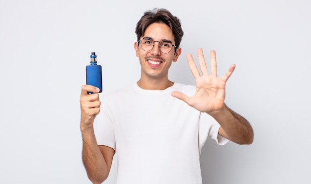 jeune homme hispanique souriant et semblant amical, montrant le numéro cinq. concept de vaporisateur de fumée