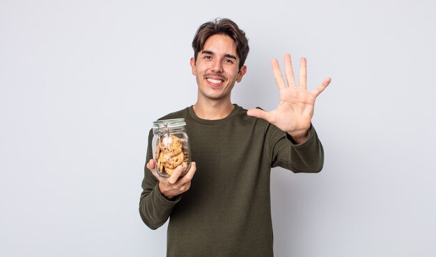 Jeune homme hispanique souriant et semblant amical, montrant le numéro cinq. notion de cookies