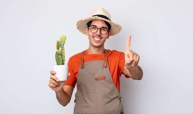 Jeune homme hispanique souriant et semblant amical, montrant le numéro un. jardinier avec concept de cactus