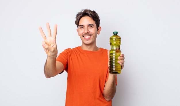 Jeune homme hispanique souriant et semblant amical, montrant le numéro trois. concept d'huile d'olive