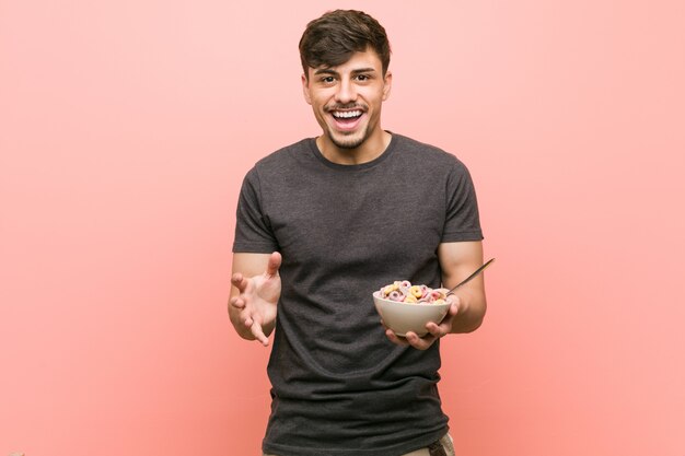 Jeune homme hispanique tenant un bol de céréales célébrant une victoire ou un succès