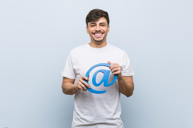 Jeune homme hispanique tenant à l'icône heureux, souriant et gai.