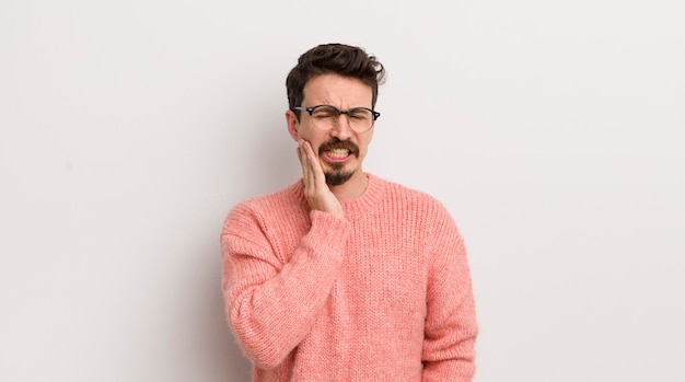 Jeune homme hispanique tenant la joue et souffrant de maux de dents douloureux se sentant malade misérable et malheureux à la recherche d'un dentiste