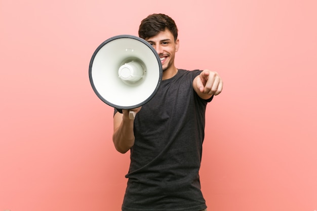 Jeune homme hispanique tenant un mégaphone des sourires gais pointant vers l'avant.