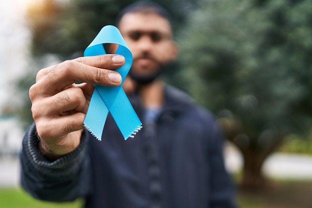 Jeune homme hispanique tenant un ruban bleu clair au parc