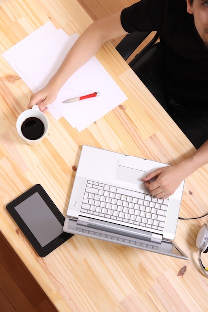 Un jeune homme hispanique travaillant sur un bureau en bois avec un ordinateur portable.