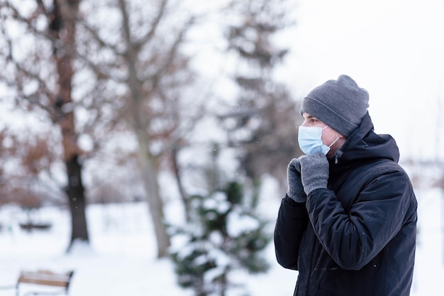 Un jeune homme en hiver porte un masque Jeune homme en masque antiviral protecteur dans la rue Le gars en vêtements d'hiver dans un masque de protection Jeune homme en vêtements chauds et écharpe un jour d'hiver